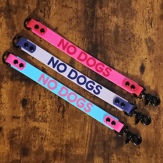 three biothane leash wraps each reading "NO DOGS" one in pink and red, one in light and dark purple, and one in light blue and pink